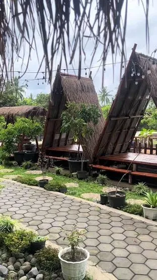 Gazebo beratap alami di antara tanaman buah dalam pot, dengan jalan setapak dan lampu gantung.